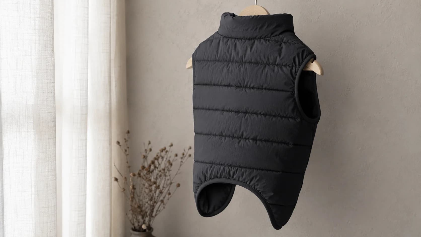 Chaqueta de plumón negra con canales horizontales colgada de una percha de madera contra una pared de yeso pálido.