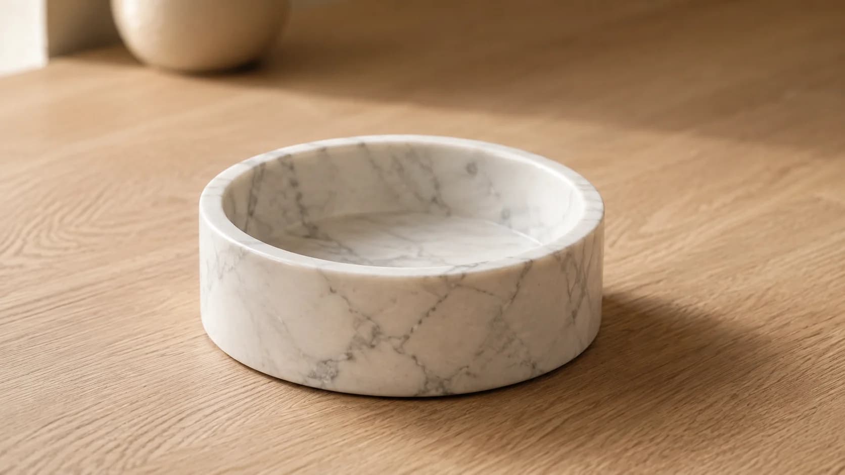 Bol de mármol de Carrara blanco con veta gris, tallado en un bloque, sobre una mesada de roble blanco aceitado.